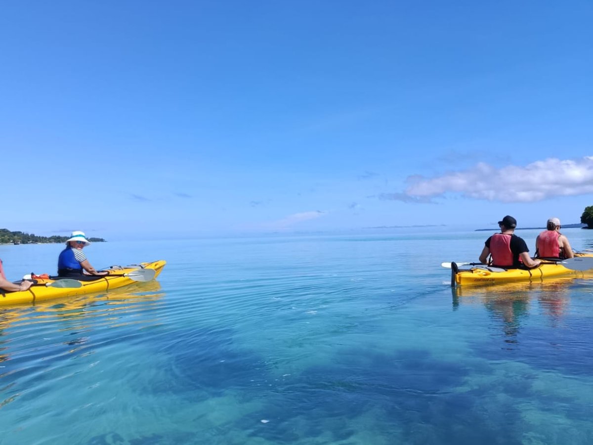 Group kayaking across clear turquoise water on the full-day tour