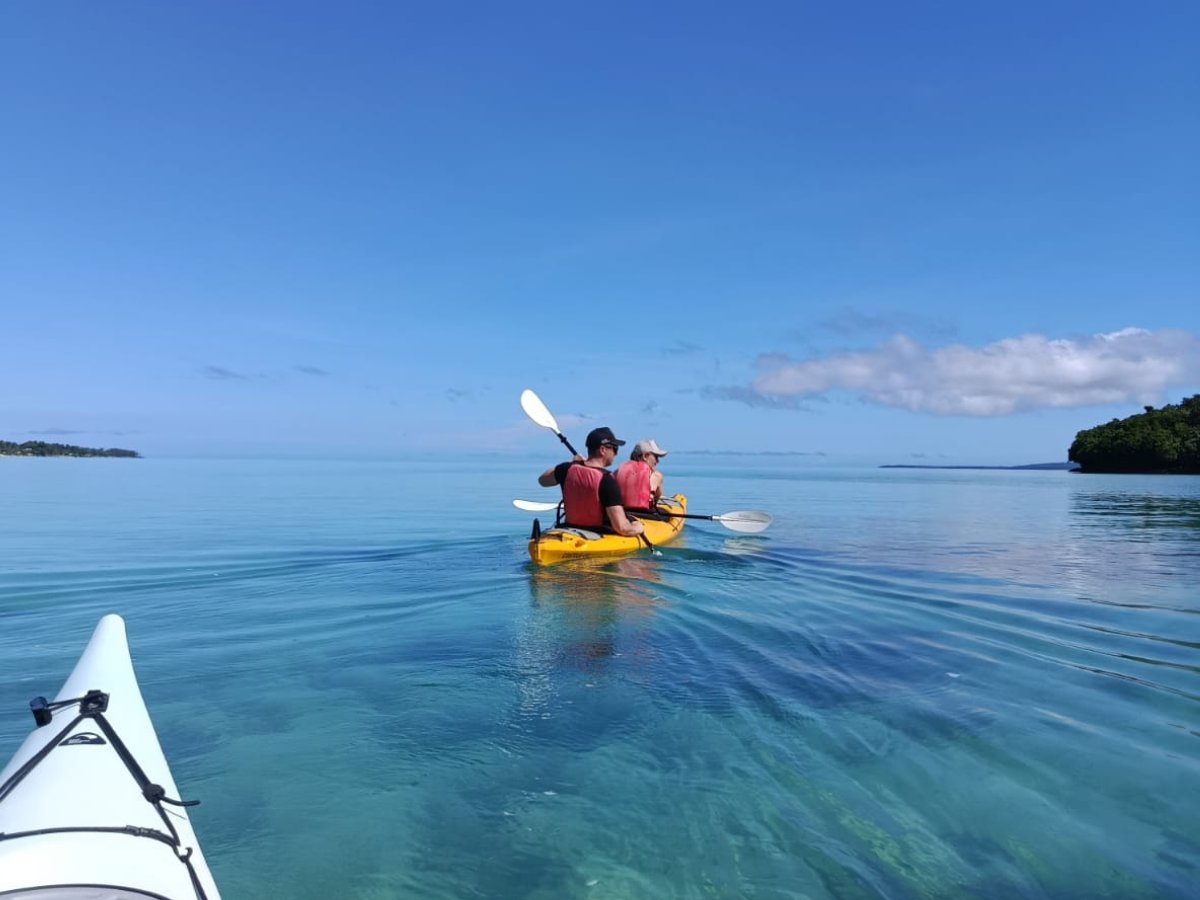 Kayakers paddling across light blue tropical waters on a coastal expedition