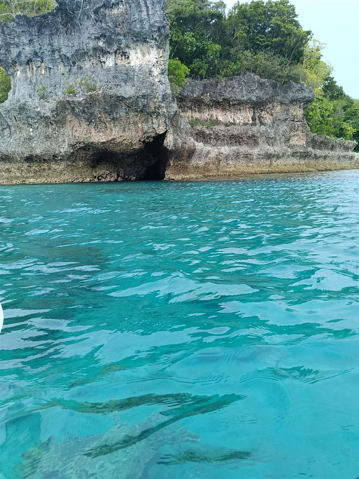 Sea cave at the foot of limestone cliffs above clear turquoise water on the way into Undine Bay