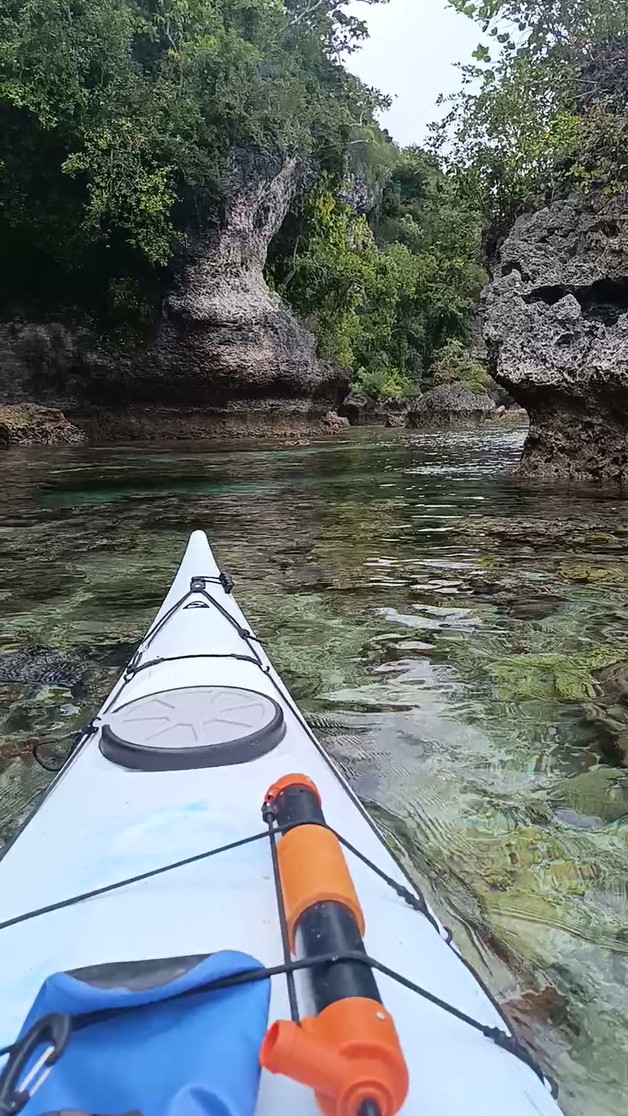 Kayak bow gliding over clear water between the limestone sea cliffs of Moso