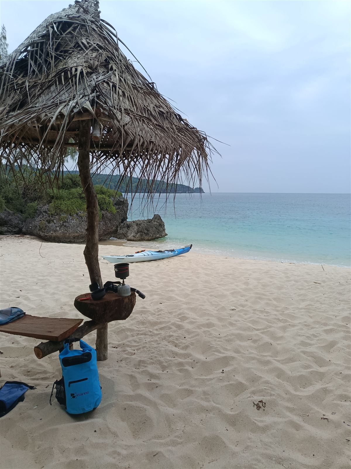 Thatched shelter on the white sand at Hapi Tok Beach, with a sea kayak pulled up by the turquoise water