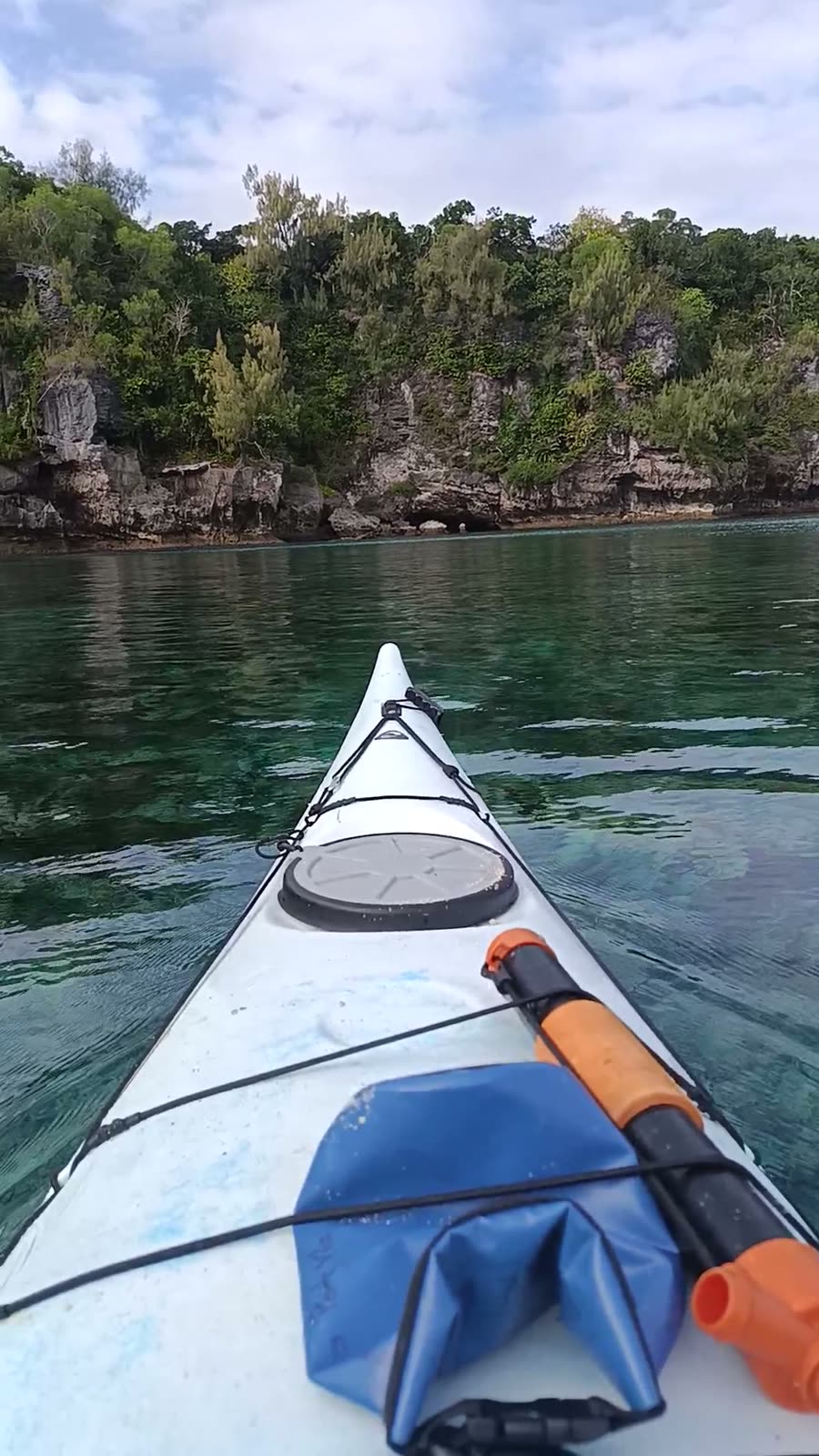 Kayak bow gliding over clear water beneath the forested limestone cliffs of Moso